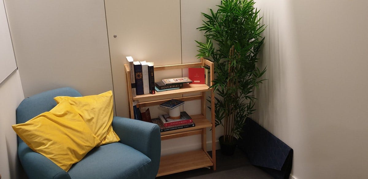 A small room with an armchair, throw cushions, a beanbag, rug, prayer mat, bookcase and pot plant.